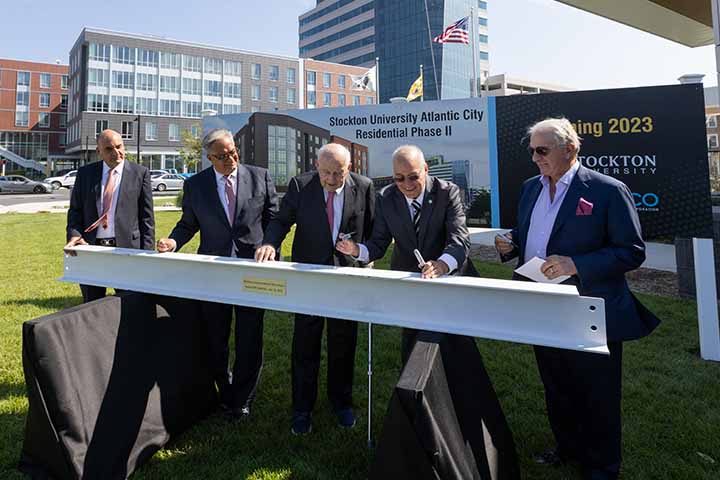 Five men sign a white steel beam