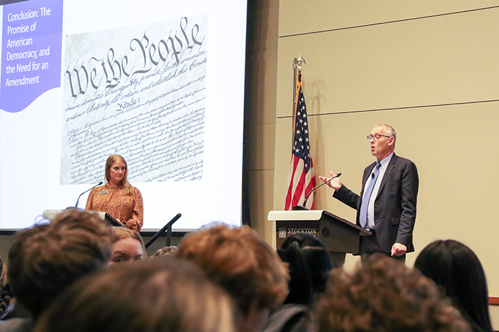 Moderator Sara Faurot stands off to the side of Richard Hasen who speaks behind a podium in the Campus Center Event Room