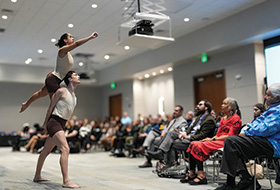 Two dancers perform in front of a seated crowd