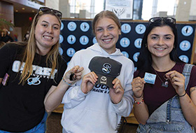 Three students holding prizes in front of a punch board