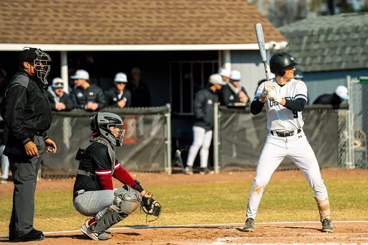 An umpire, baseball catcher squatting, and Jordan Nitti in white Stockton uniform up at bat