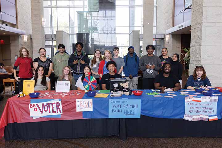 A group of students in the Campus Center Grand Hall with signage promoting registering for voting