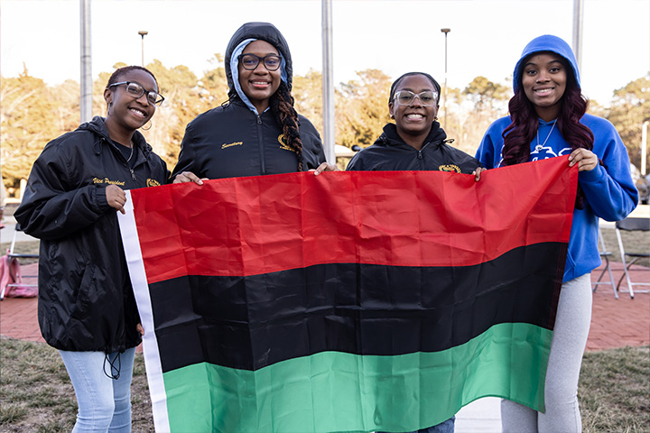 Four Stockton students hold up the Pan African flag, which features three horizontal stripes of red, black and green