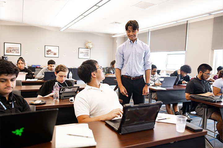 Dylan Gutowski converses with one of many students seated in a classroom with laptops