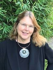 A woman wearing glasses, smiling at the camera standing in front of a tree.