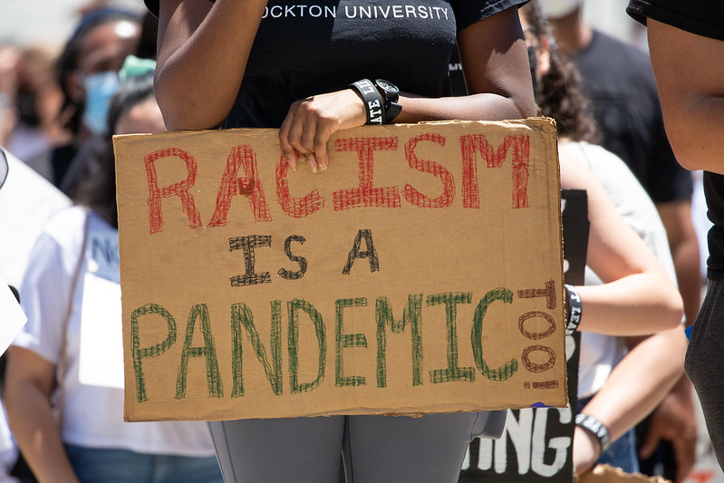 Protesters holding up a sign stating: "Racism is a Pandemic, too!"