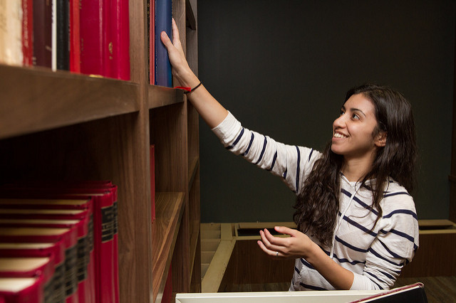 A student in a library reaching for a book on a shelf