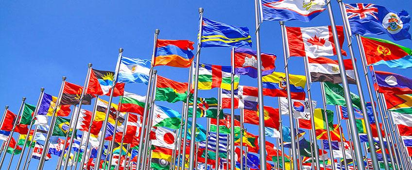 Photo of World Flags on flagpole moving with the wind, set against a blue sky.
