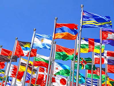 Flags from various countries blowing in the wind against a blue sky.