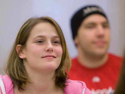 A student with short hair and wearing a pink shirt smiling at the camera.