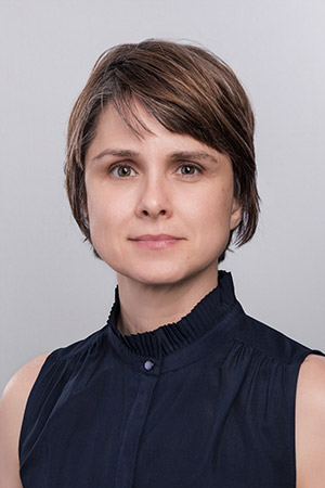 Elizabeth Throesch smiling at the camera in front of a gray background.