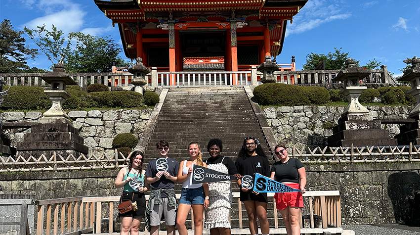 The students posing in front of a temple holding Stockton signs