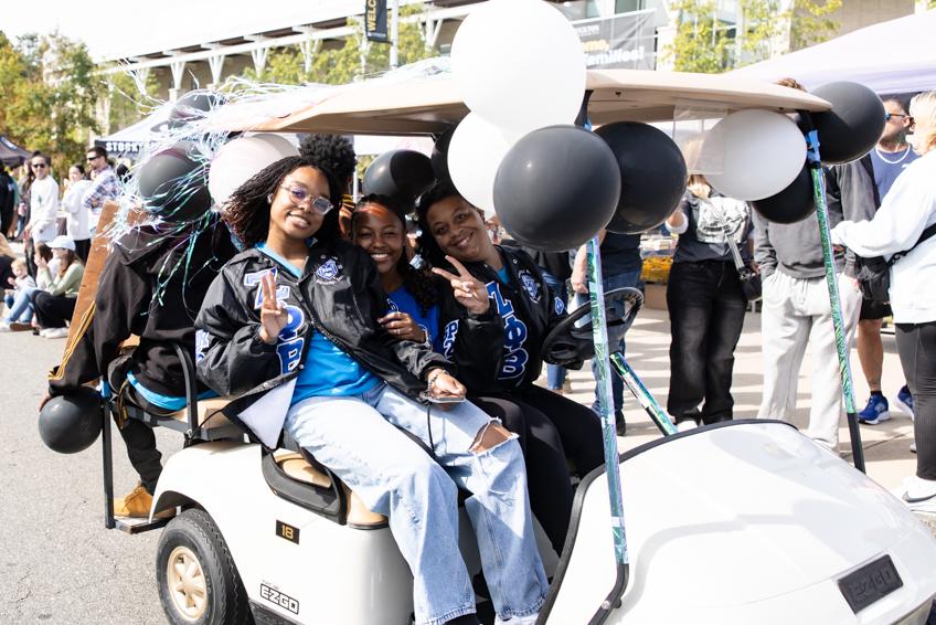 students on university weekend golf cart smiling and waving