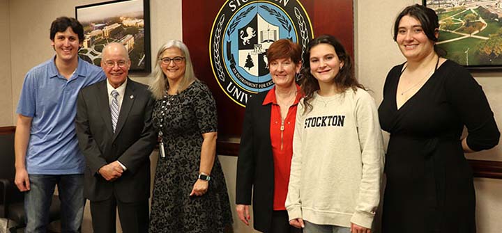 Harvey Kesselman and the Glass family post in front of the University seal in the President's Conference Room