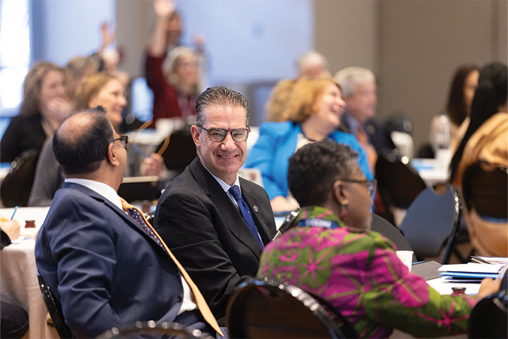 Michael Palladino smiling while sitting at a round table among faculty and staff